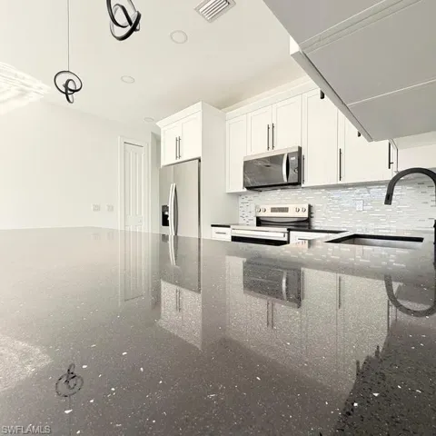 Kitchen featuring white cabinets, dark stone counters, stainless steel appliances, and pendant lighting