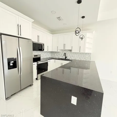 Kitchen featuring stainless steel appliances, dark stone countertops, hanging light fixtures, white cabinets, and tasteful backsplash