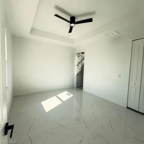 Empty room featuring a tray ceiling, light marble finish flooring, and a ceiling fan