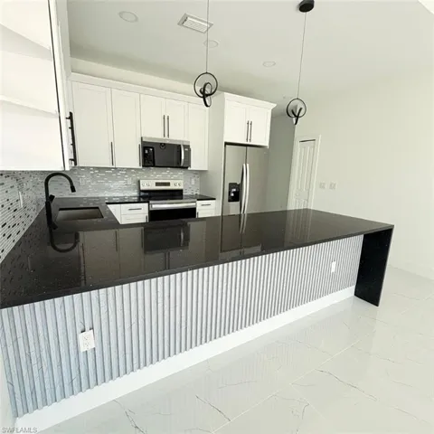 Kitchen featuring dark stone countertops, stainless steel appliances, a peninsula, and white cabinetry