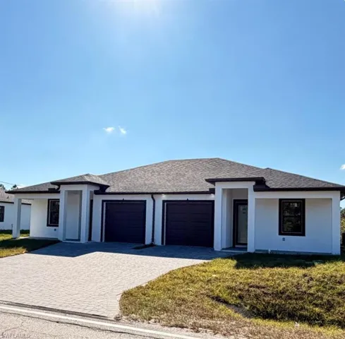 Prairie-style house featuring a front lawn, decorative driveway, an attached garage, stucco siding, and roof with shingles