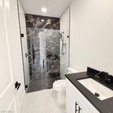 Bathroom featuring a marble finish shower, vanity, light marble finish flooring, and recessed lighting