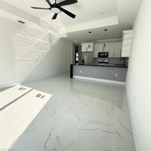 Unfurnished living room featuring a ceiling fan, a raised ceiling, light marble finish floors, and recessed lighting