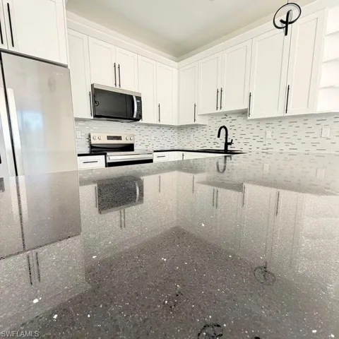 Kitchen featuring white cabinets, stainless steel appliances, dark stone countertops, tasteful backsplash, and open shelves