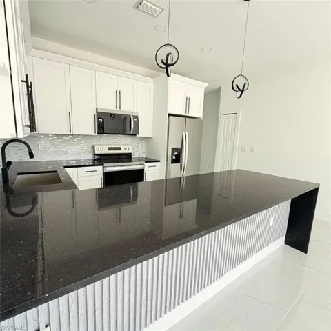 Kitchen with dark stone countertops, stainless steel appliances, white cabinets, tasteful backsplash, and a peninsula