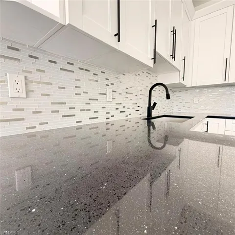 Kitchen view of dark stone counters, white cabinets, and tasteful backsplash