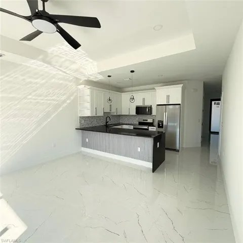 Kitchen with stainless steel appliances, light marble finish floors, backsplash, hanging light fixtures, and white cabinetry