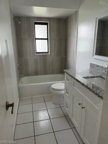 Full bathroom with tile flooring, tiled shower / bath combo, vanity, and toilet