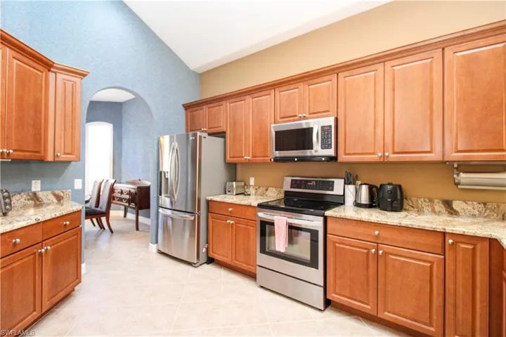 Kitchen featuring light stone counters, appliances with stainless steel finishes, light tile patterned floors, and high vaulted ceiling