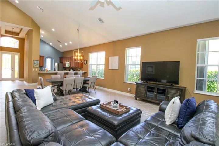 Living room featuring ceiling fan with notable chandelier, light tile patterned floors, and high vaulted ceiling