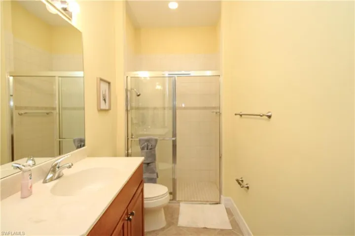 Bathroom featuring tile patterned flooring, a shower with door, toilet, and vanity