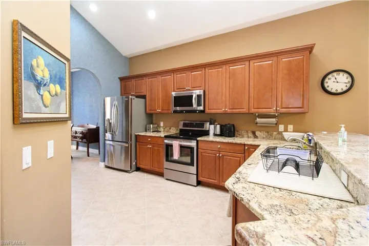 Kitchen featuring sink, light stone countertops, appliances with stainless steel finishes, lofted ceiling, and light tile patterned floors