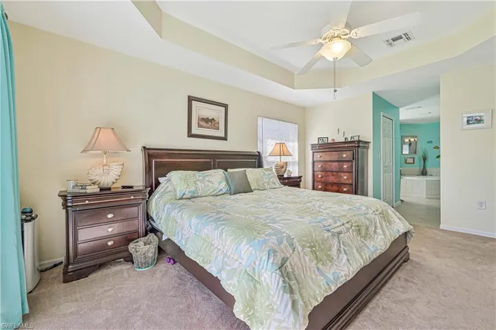 Carpeted bedroom with ceiling fan, ensuite bath, and a raised ceiling