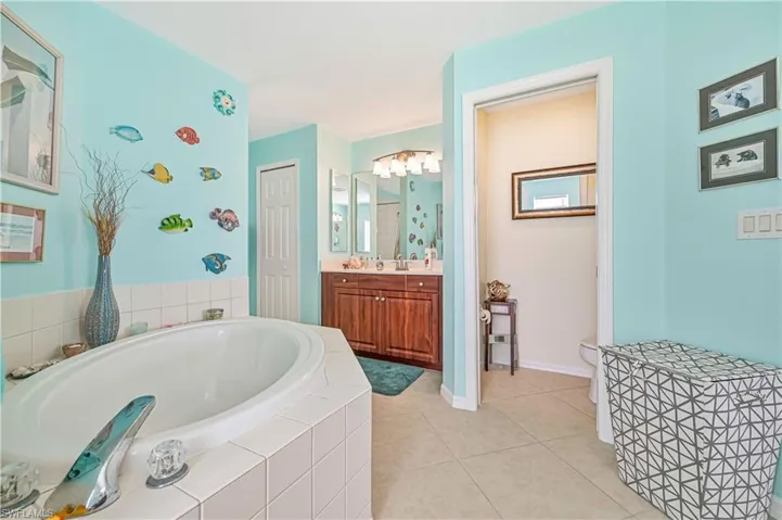 Bathroom with vanity, Private toilet with pocket door, a relaxing tiled tub, tile floors, and an inviting Lighting fixture.