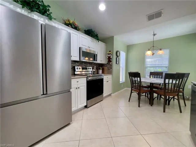 Kitchen featuring light tile patterned floors, decorative backsplash, stainless steel appliances, and newly updated white cabinets