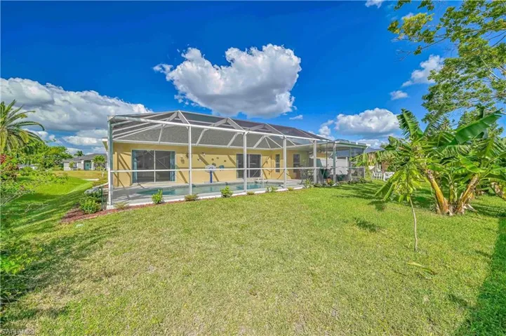 Rear view of property featuring Screened enclosure and a lawn