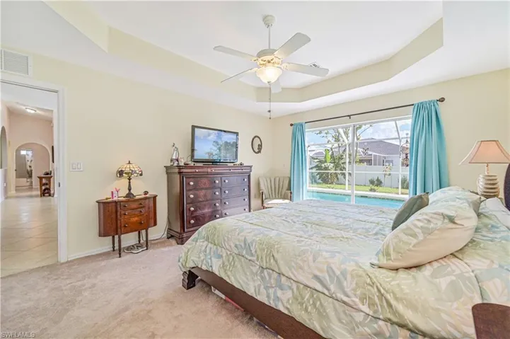 Carpeted bedroom featuring ceiling fan, a raised ceiling, and access to Pool area and back yard.