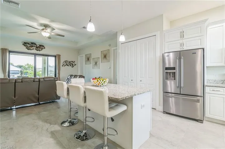 Kitchen with stainless steel fridge with ice dispenser, open floor plan, light stone countertops, white cabinets, and a kitchen bar