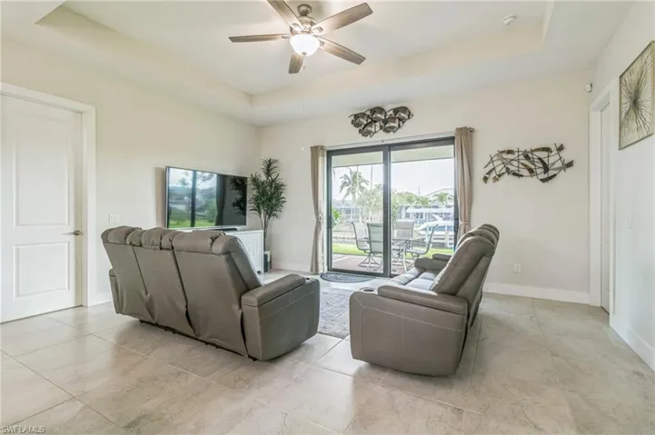 Living area featuring a raised ceiling, ceiling fan, light tile patterned floors, and baseboards