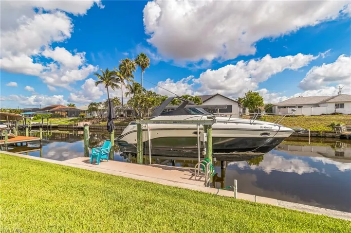 Dock area with boat lift, a water view, a lawn, and a residential view