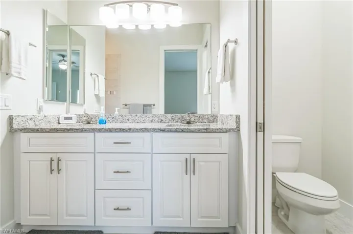 Full bathroom with toilet, double vanity, baseboards, and ceiling fan