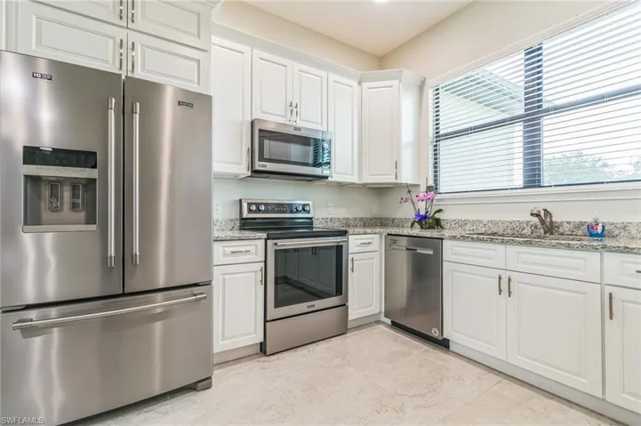 Kitchen featuring stainless steel appliances, white cabinetry, light stone countertops, and a sink