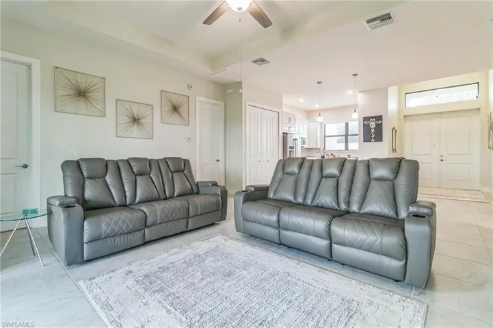 Living area featuring ceiling fan, a raised ceiling, and light tile patterned floors