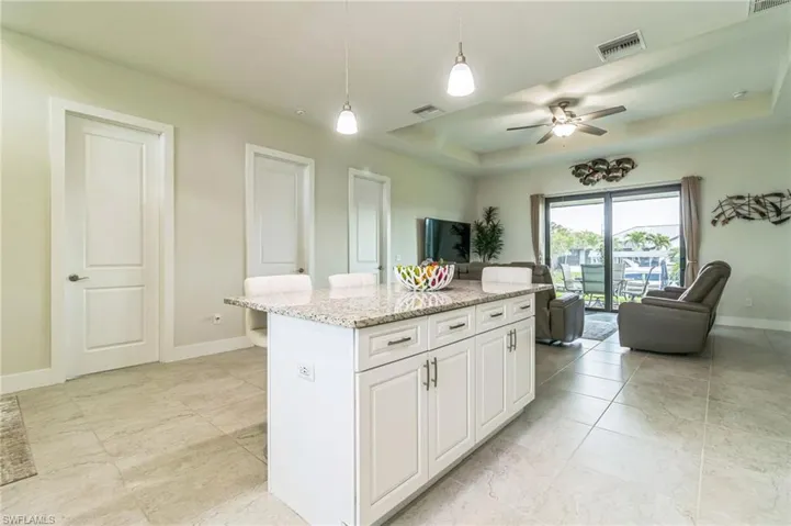 Kitchen with ceiling fan, open floor plan, hanging light fixtures, baseboards, and light stone countertops