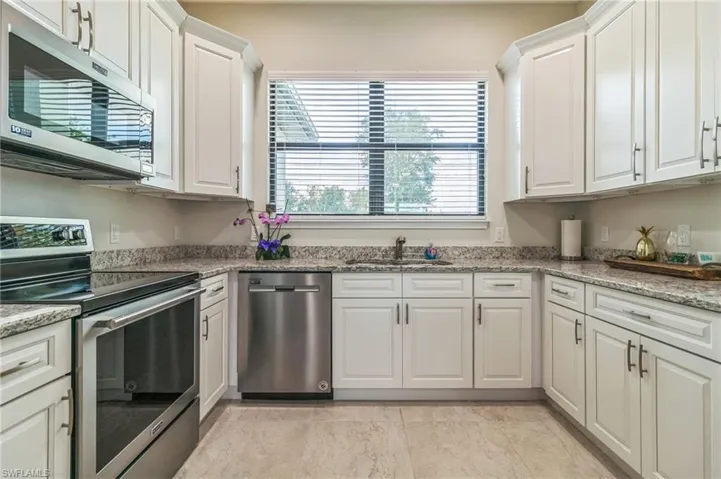 Kitchen with appliances with stainless steel finishes, a sink, white cabinetry, and light stone countertops