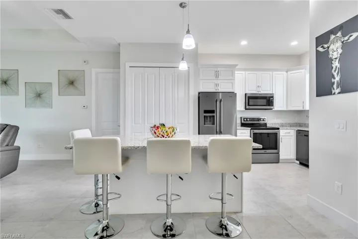Kitchen featuring stainless steel appliances, a kitchen breakfast bar, light stone counters, white cabinetry, and recessed lighting