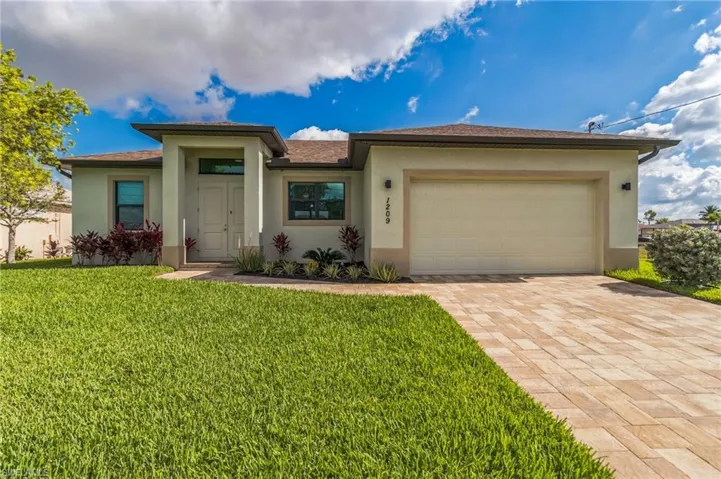 View of front of home with stucco siding, a front yard, decorative driveway, and an attached garage