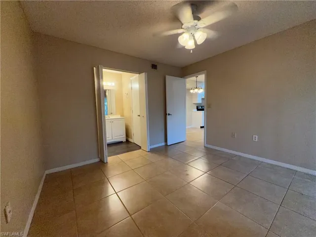Unfurnished bedroom featuring a textured ceiling, a ceiling fan, a chandelier, light tile patterned floors, and ensuite bath
