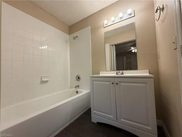 Bathroom with vanity, shower / bath combination, a textured ceiling, dark wood finished floors, and a textured wall