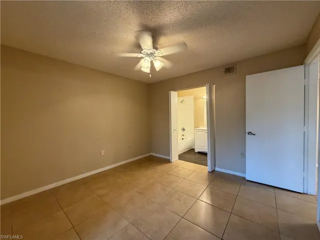 Unfurnished bedroom with a textured ceiling, a ceiling fan, ensuite bath, and light tile patterned floors
