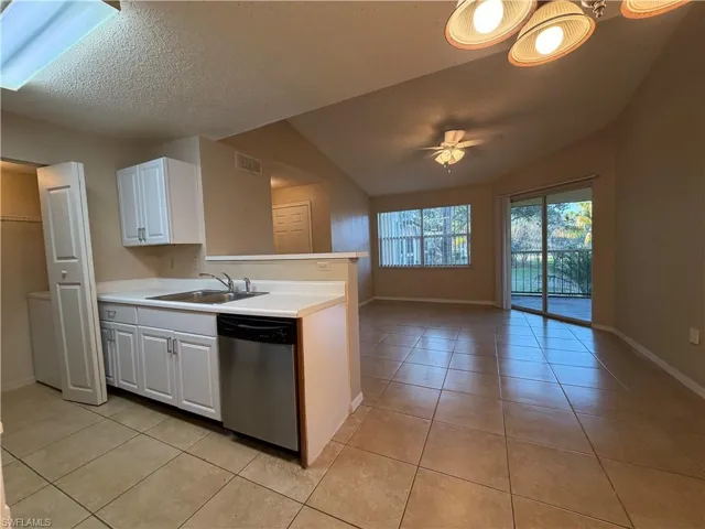 Kitchen featuring stainless steel dishwasher, white cabinetry, light tile patterned floors, and light countertops