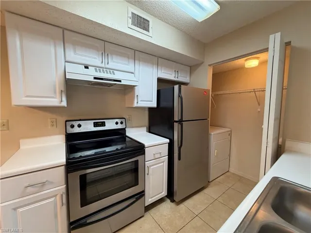 Kitchen with stainless steel appliances, a textured ceiling, white cabinets, light countertops, and light tile patterned floors