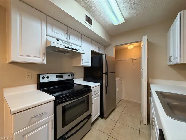 Kitchen featuring stainless steel appliances, light countertops, a textured ceiling, white cabinetry, and washer and dryer