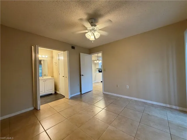 Unfurnished bedroom with a textured ceiling, a ceiling fan, light tile patterned flooring, ensuite bath, and suspended lighting