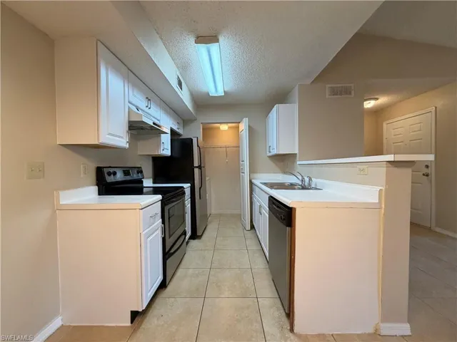 Kitchen with stainless steel appliances, a textured ceiling, white cabinets, and light countertops