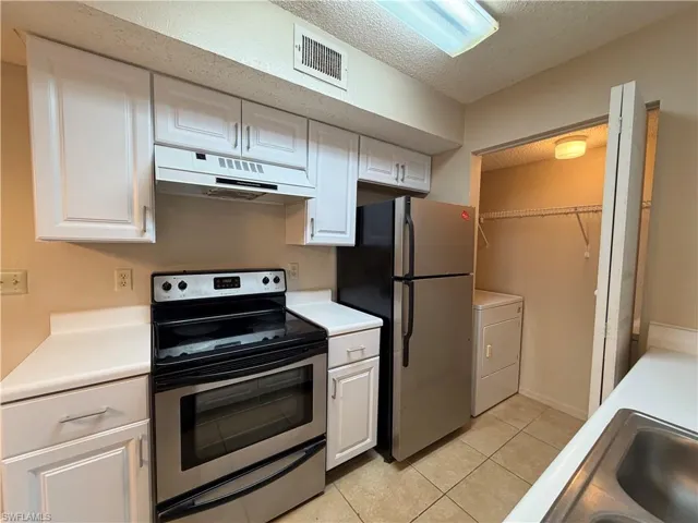Kitchen featuring stainless steel appliances, a textured ceiling, light countertops, white cabinetry, and light tile patterned floors