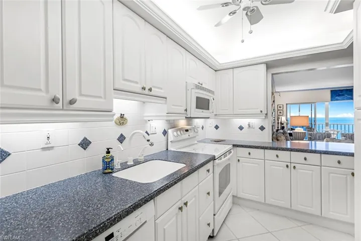 Kitchen with sink, white cabinetry, decorative backsplash, and white appliances