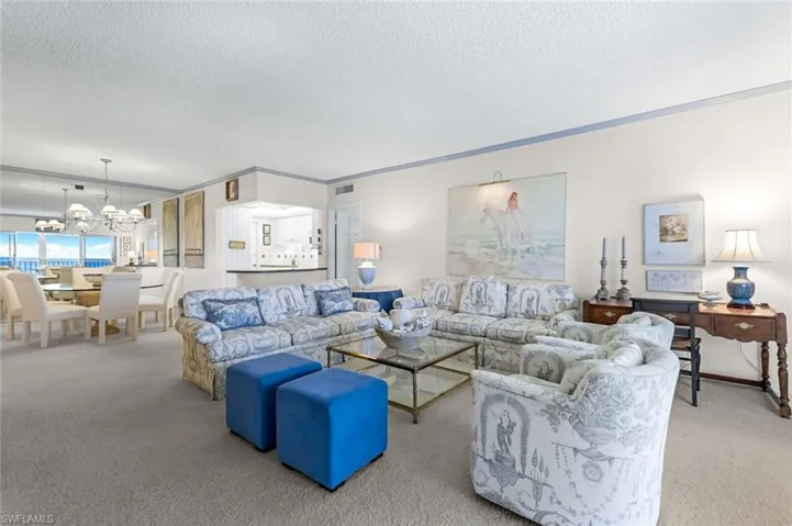 Carpeted living room with a textured ceiling, a notable chandelier, and ornamental molding