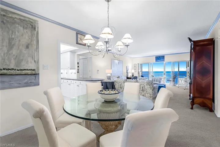 Dining space with light carpet, crown molding, and a chandelier