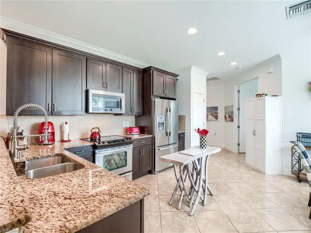 Kitchen with dark brown cabinetry, light stone counters, stainless steel appliances, tasteful backsplash, and sink