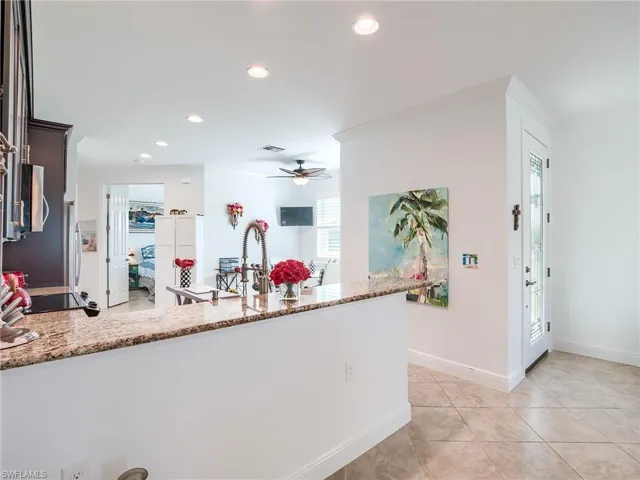 Kitchen featuring light stone countertops, kitchen peninsula, dark brown cabinets, ceiling fan, and light tile floors