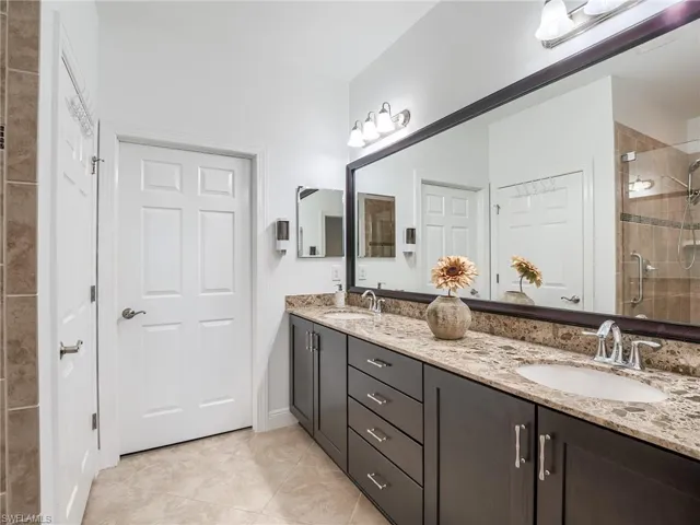 Bathroom with a shower with shower door, oversized vanity, double sink, and tile floors