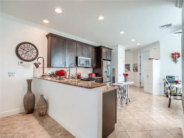 Kitchen with dark brown cabinets, tasteful backsplash, stone counters, light tile floors, and appliances with stainless steel finishes