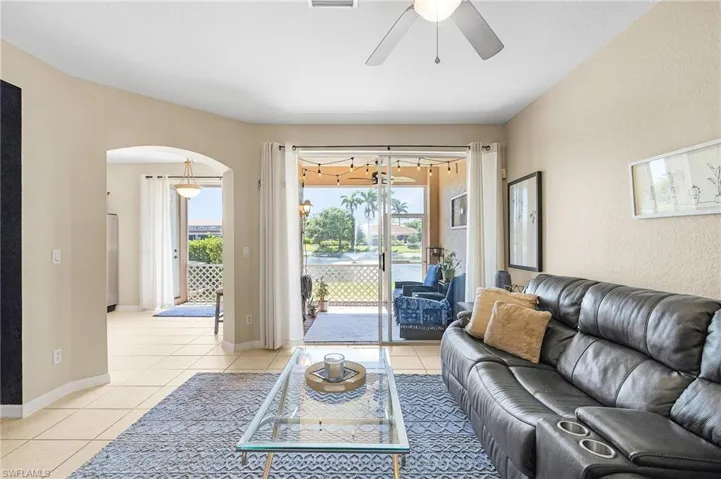 Living room with arched walkways, light tile patterned floors, ceiling fan, and baseboards