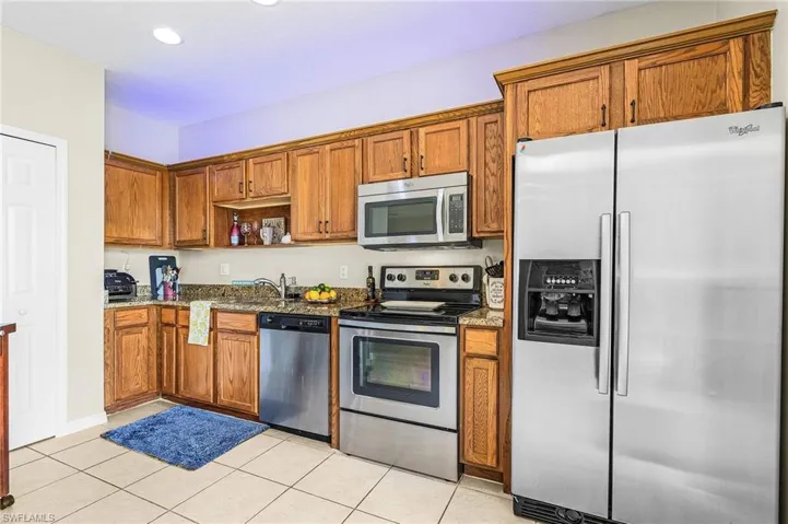 Kitchen featuring appliances with stainless steel finishes, brown cabinets, dark stone counters, light tile patterned floors, and recessed lighting