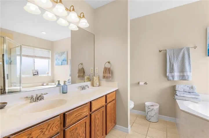 Full bath featuring a garden tub, a stall shower, double vanity, tile patterned floors, and toilet